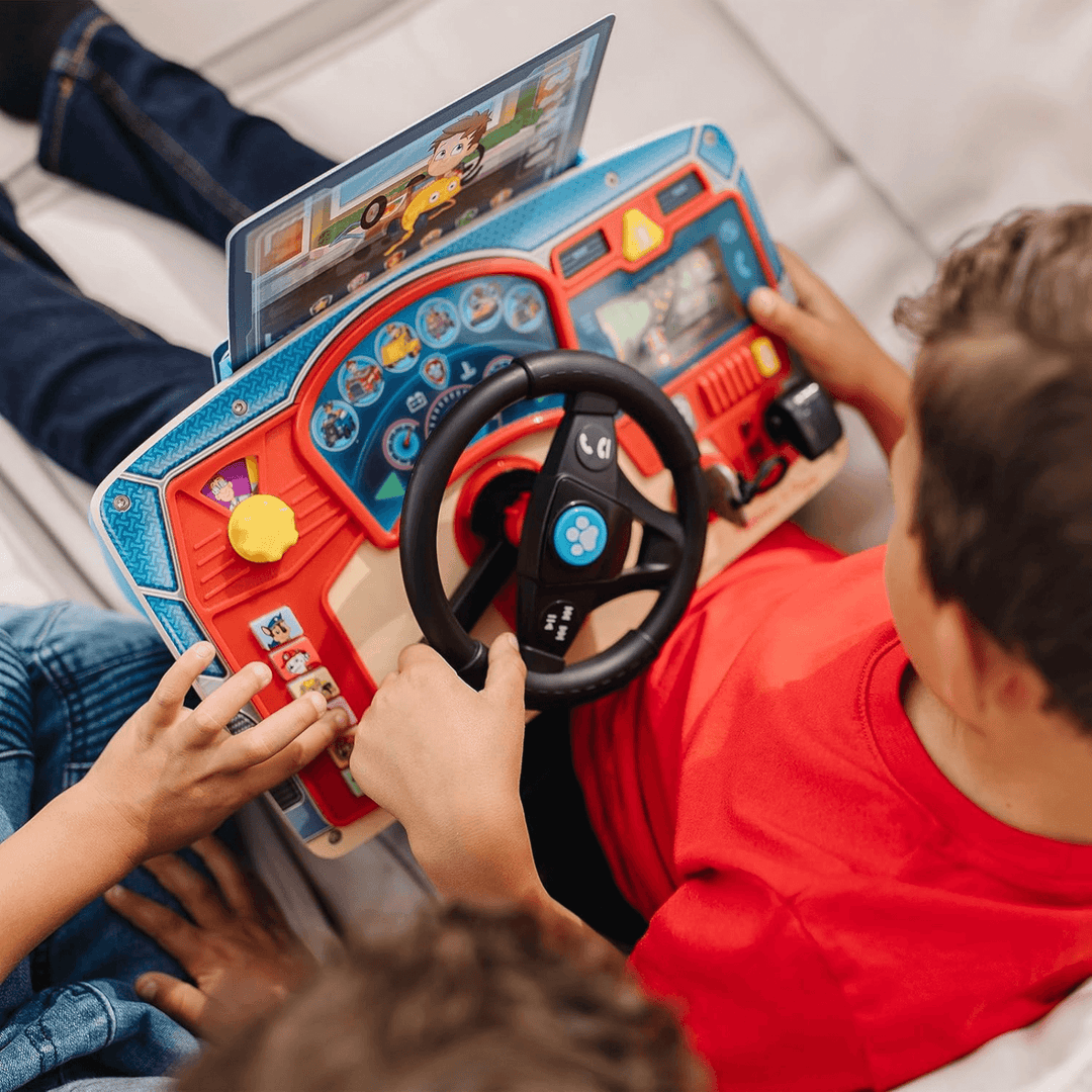little boy sits on sofa beside friend as they play with the dashboard and steering wheel
