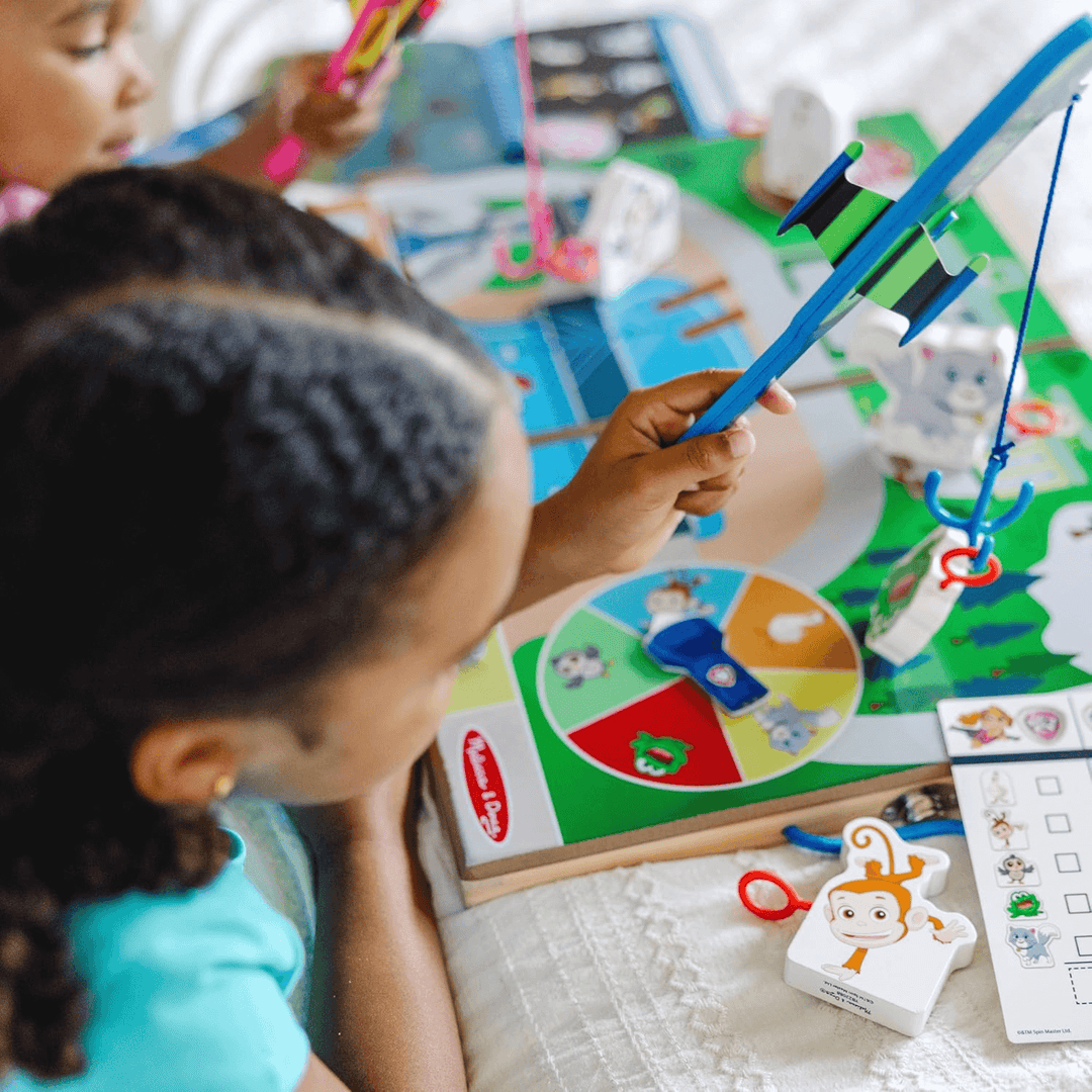 detail shot of little girl holding airplane with fishing hook securing wooden frog on activity board