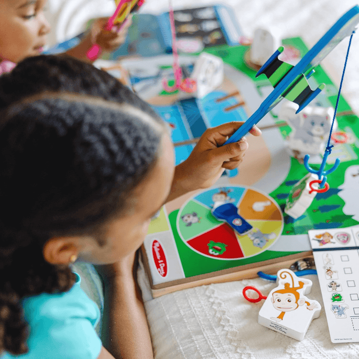 detail shot of little girl holding airplane with fishing hook securing wooden frog on activity board