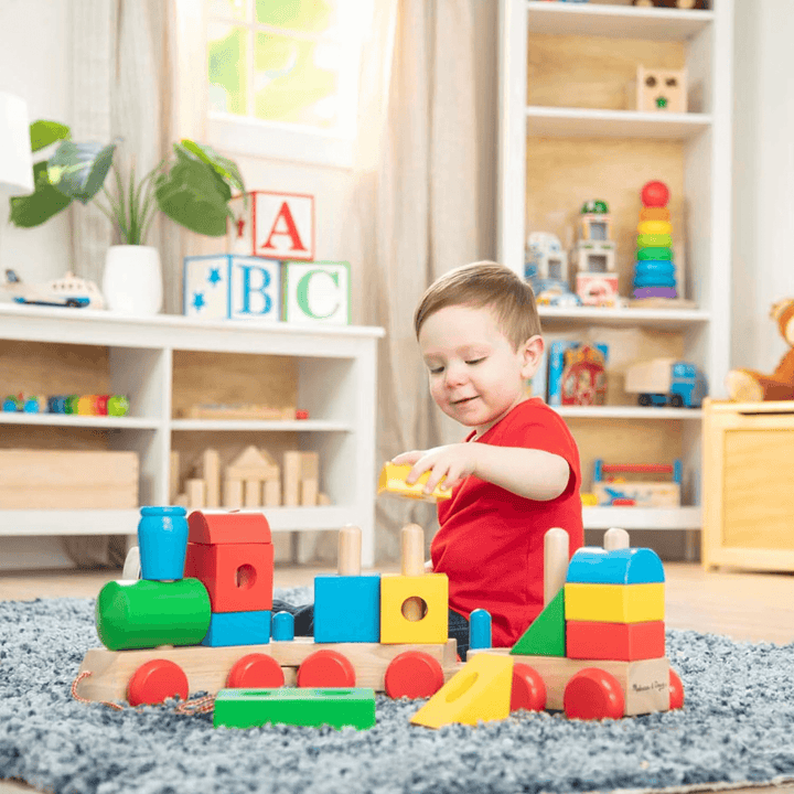little boy stacks yellow block onto train as he plays in his bedoom