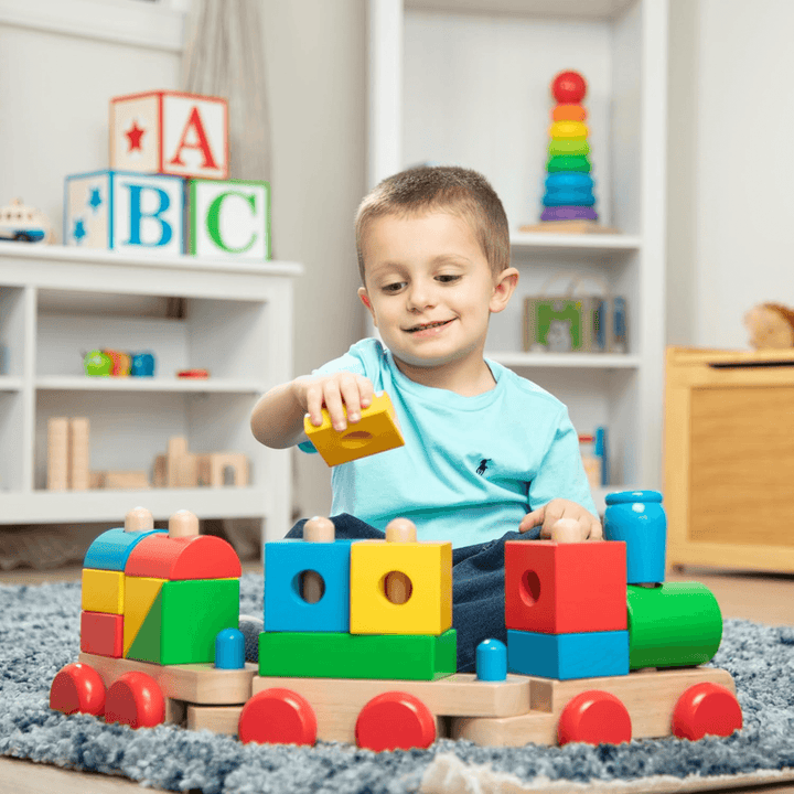 little boy adds yellow block to train set in bedroom