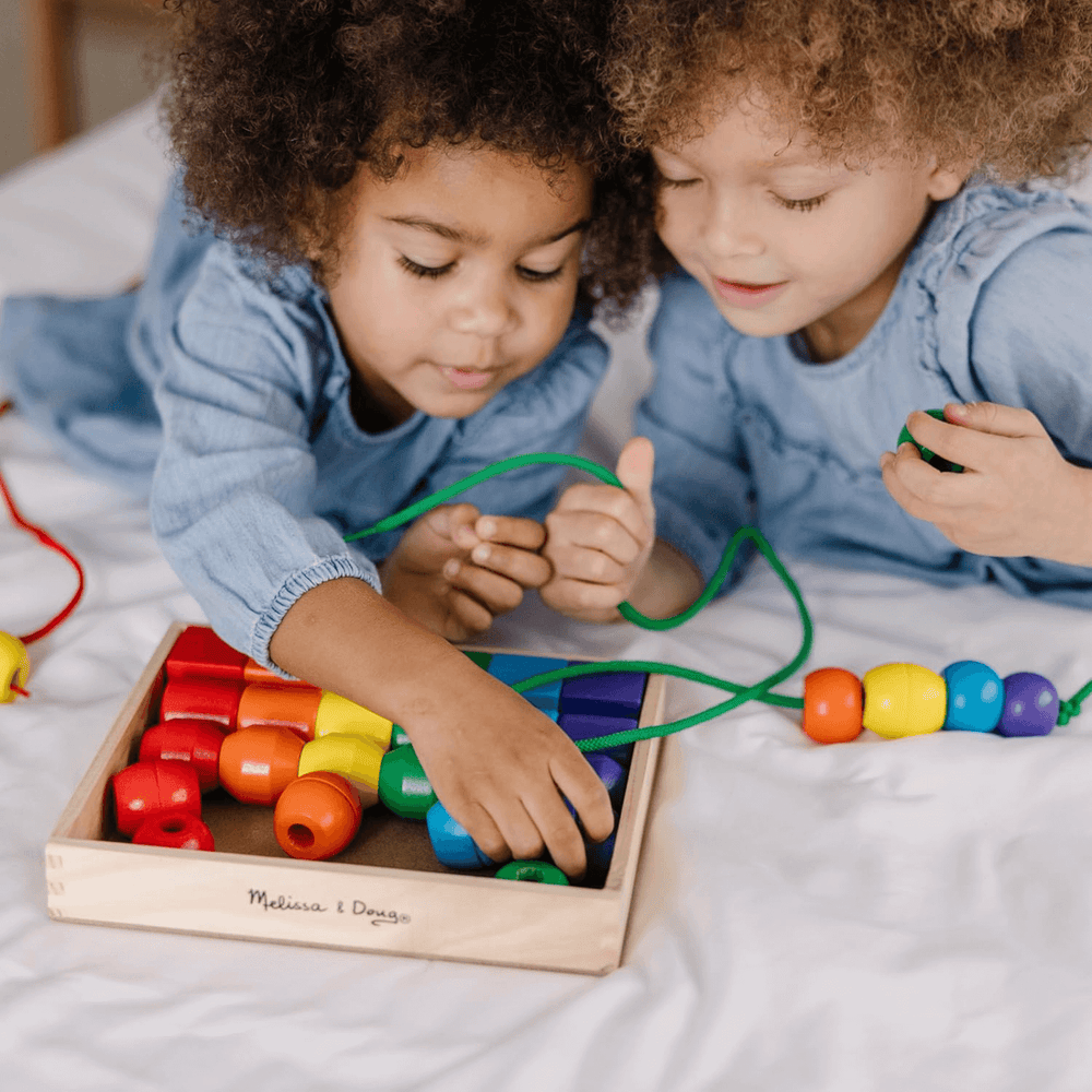 two little girls playing with green lacing string and blue coloured wooden beads
