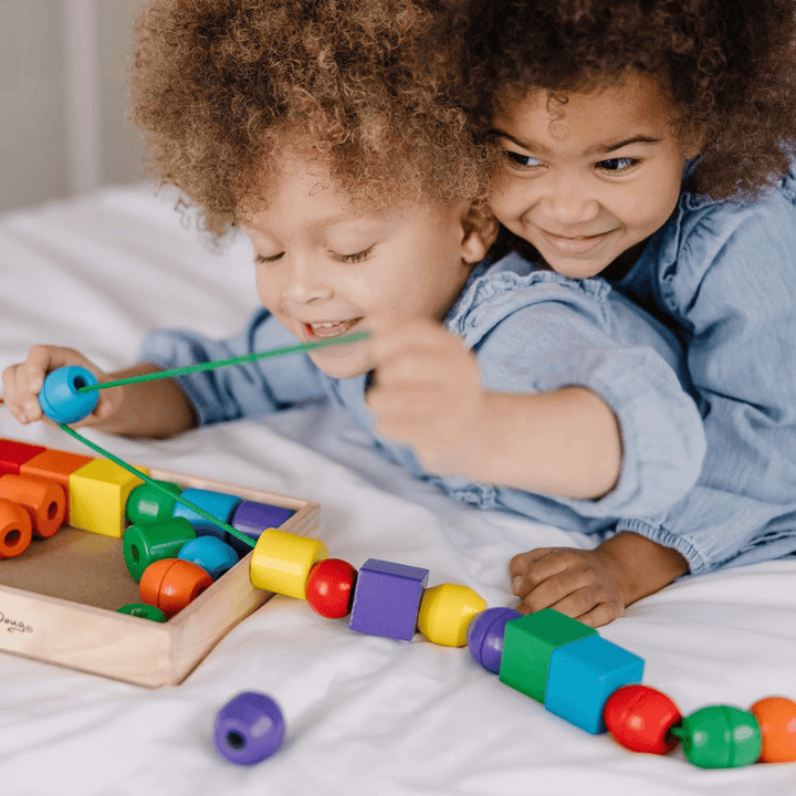 two young girls smile as they play with the wooden lacing bead set