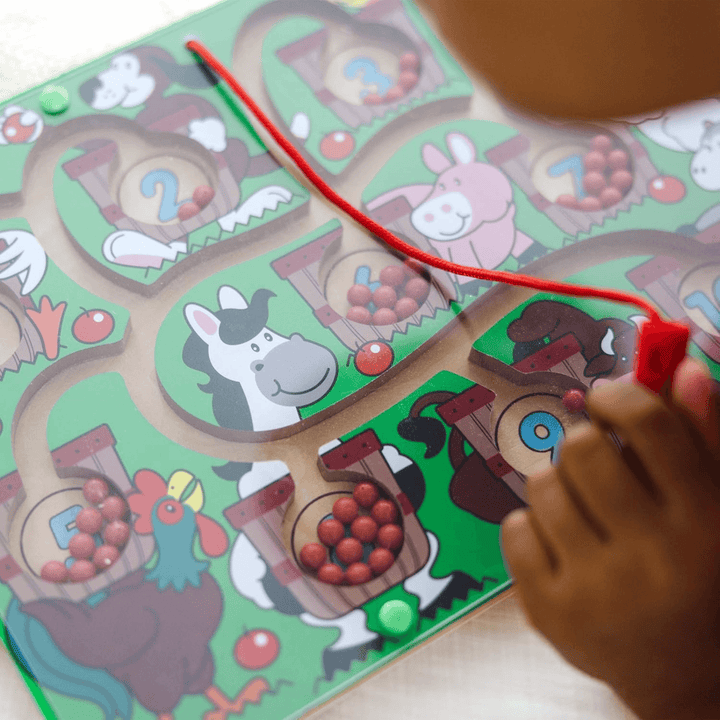 child's hand holds red magnetic wand to move red apple to a basket number