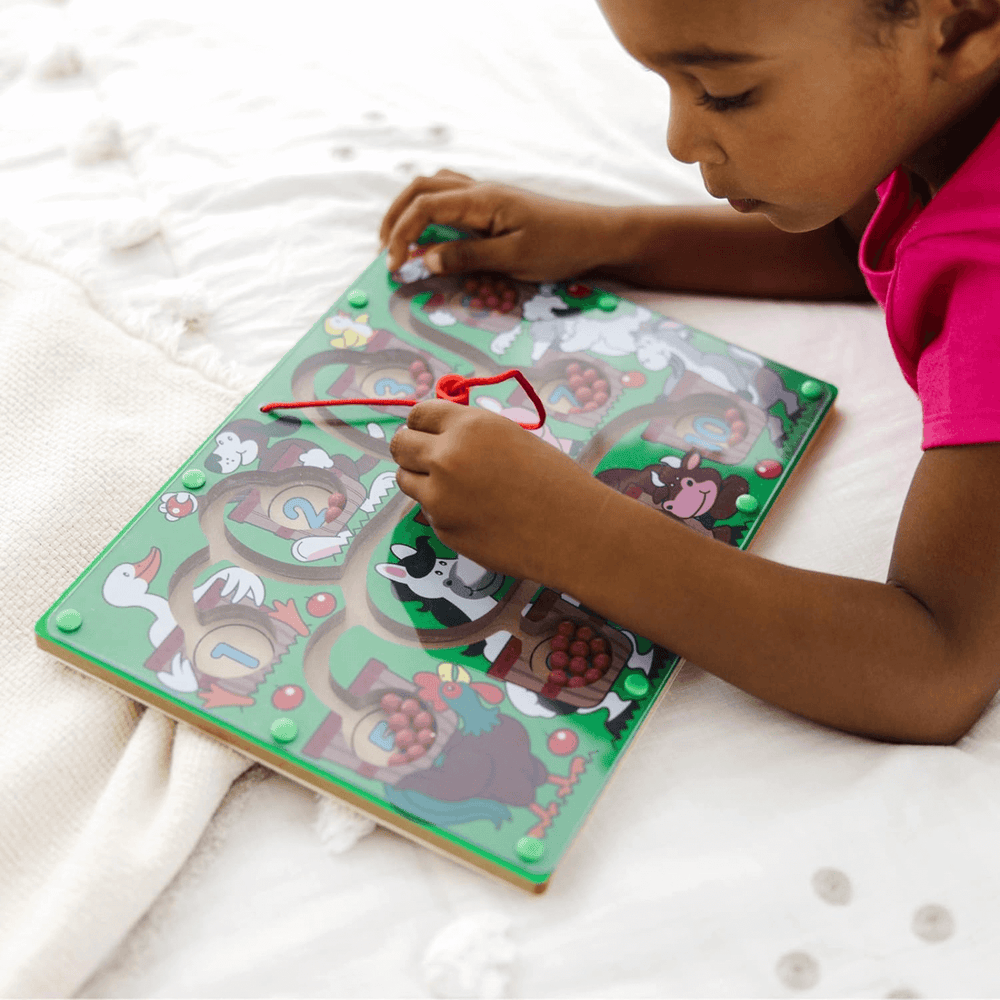 detail shot of little girl concentrating as she moves red apple to basket with magnetic red wand
