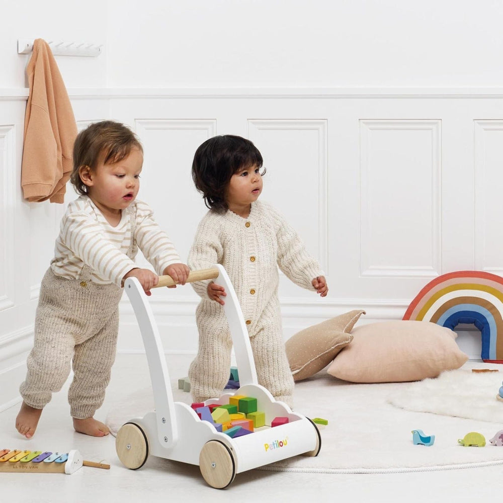 Two children playing with a wooden walker toy in a room with a rainbow decoration.