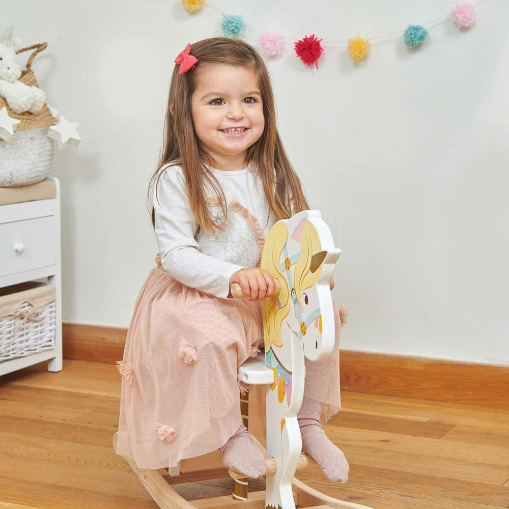 Child sitting on a rocking horse in a nursery with colorful decorations on the wall.