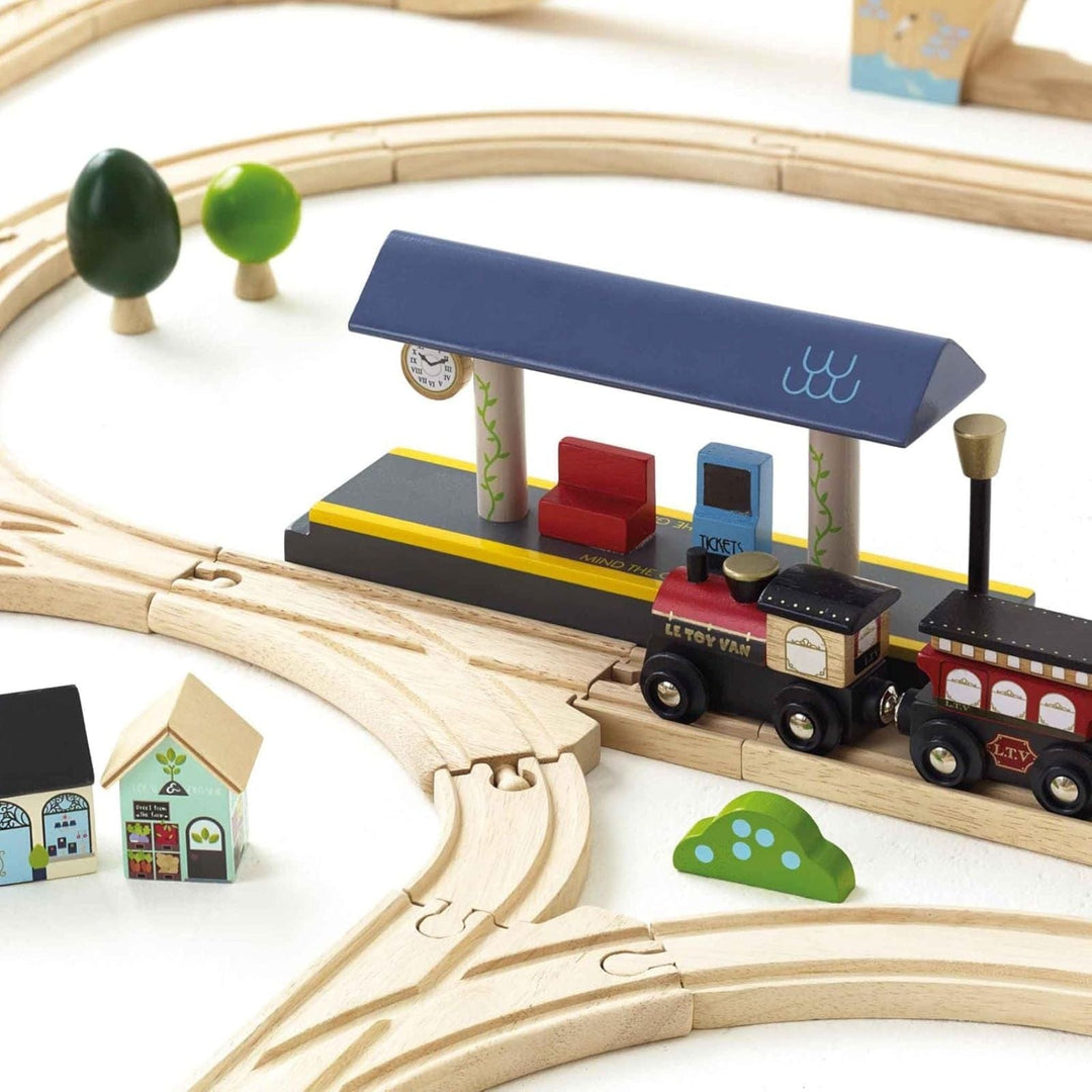 Wooden toy train set with tracks, train, and small buildings on a white background
