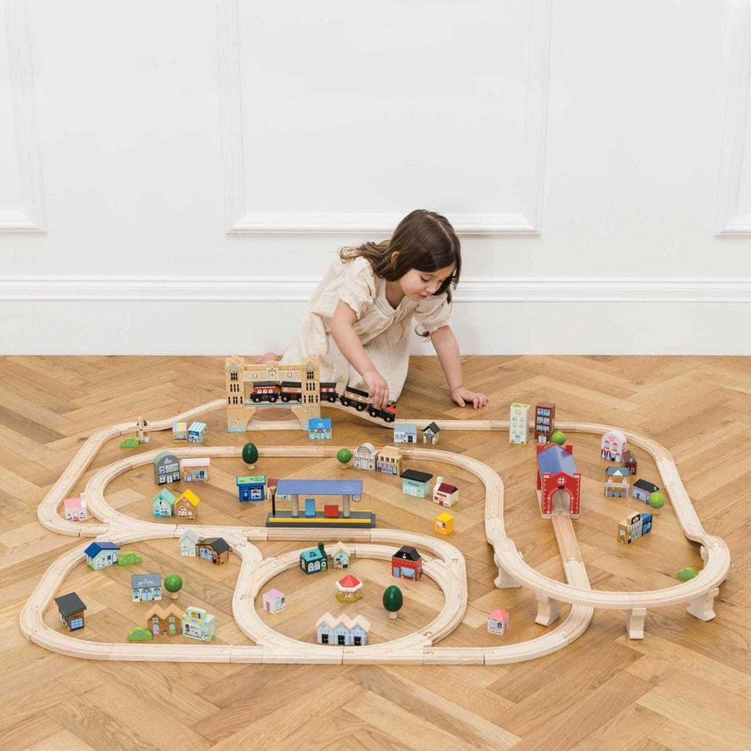 little girl playing with wooden train set in room with wooden floor and white panelled walls