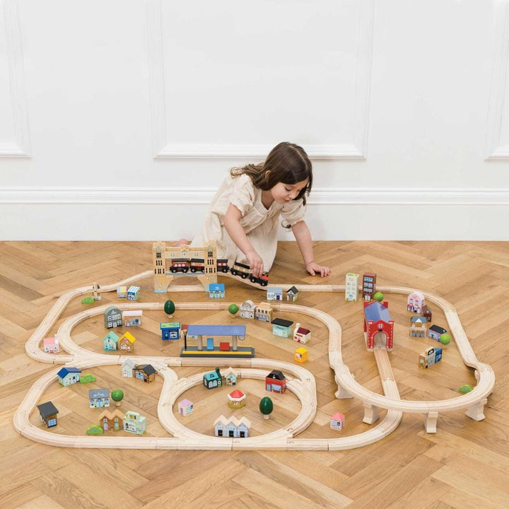 little girl playing with wooden train set in room with wooden floor and white panelled walls