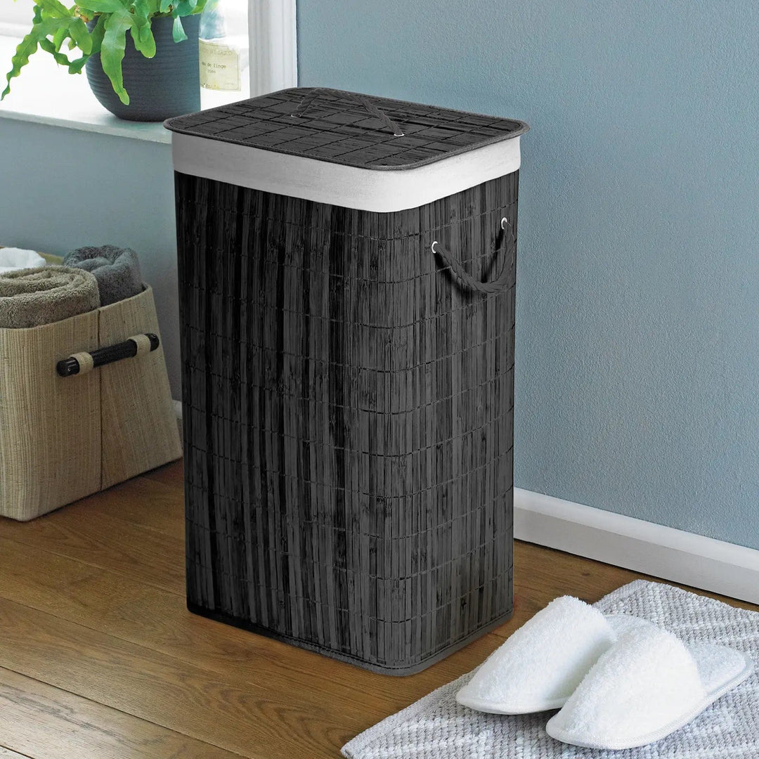 Charcoal grey, natural bamboo laundry basket with white rope handles, in a bathroom with slippers and towel storage