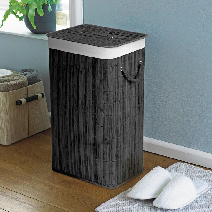 Charcoal grey, natural bamboo laundry basket with white rope handles, in a bathroom with slippers and towel storage