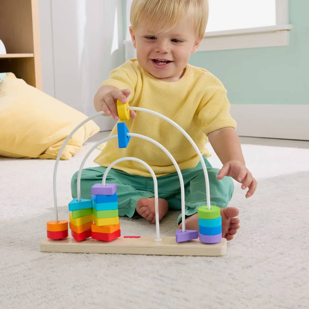 Child playing with a colourful rainbow toy arch on a carpeted floor.