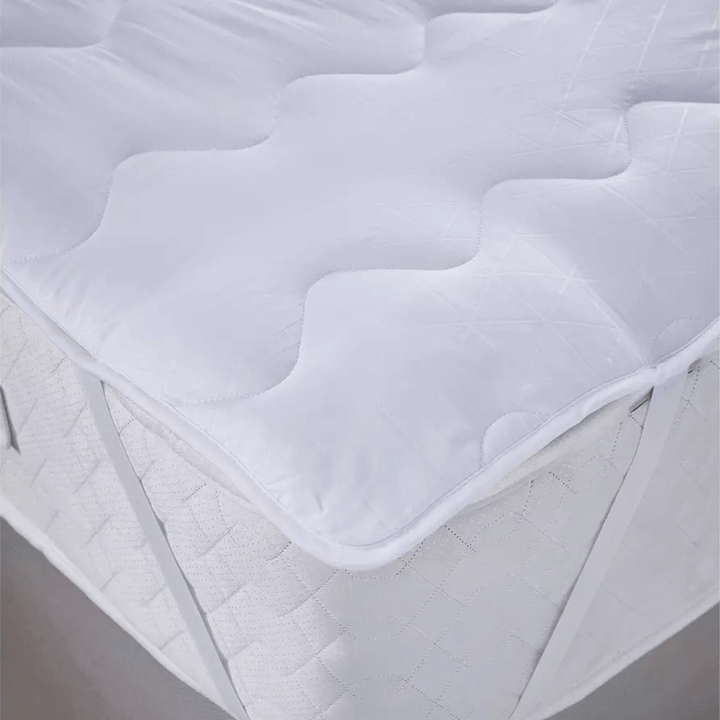White mattress pad on a bed with a neutral background