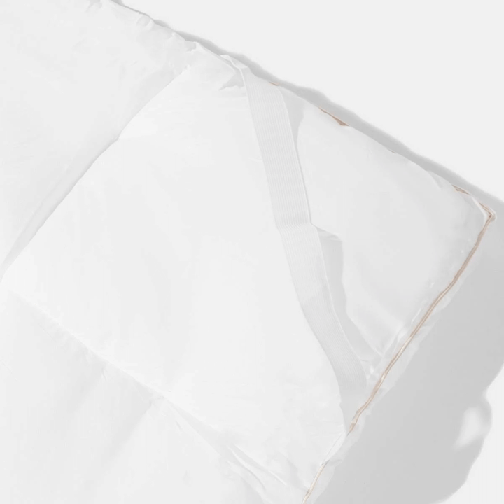 Close-up of a white comforter with gold trim on a light gray background