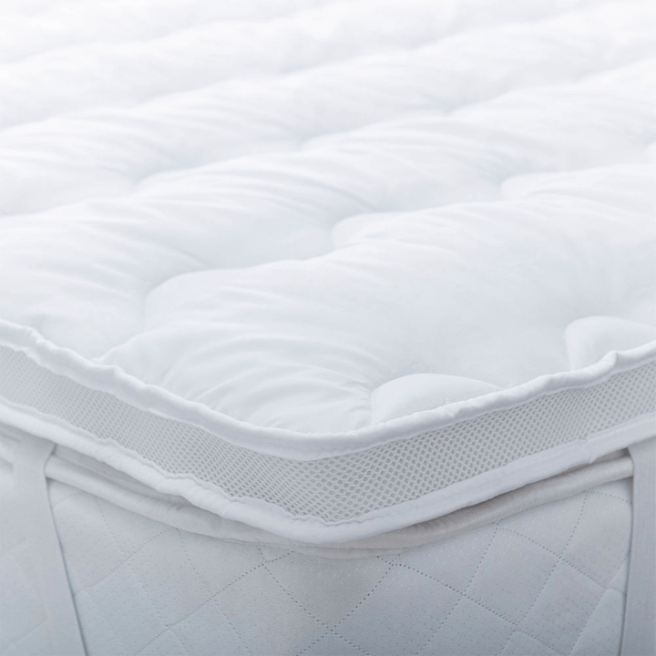 Close-up of a white quilted mattress cover on a bed with air mesh sides