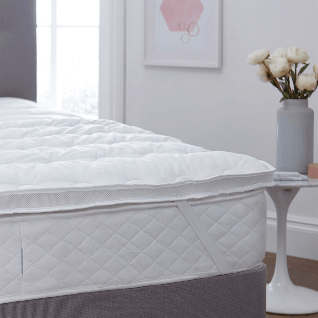 Mattress protector on a bed in a bedroom with a vase of flowers on a table.