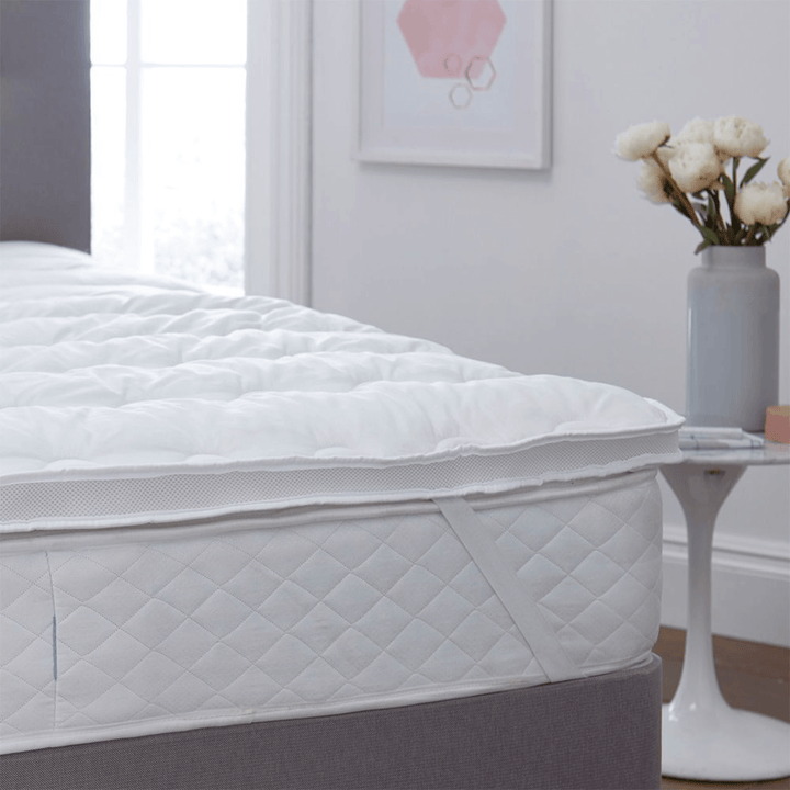 Mattress protector on a bed in a bedroom with a vase of flowers on a table.