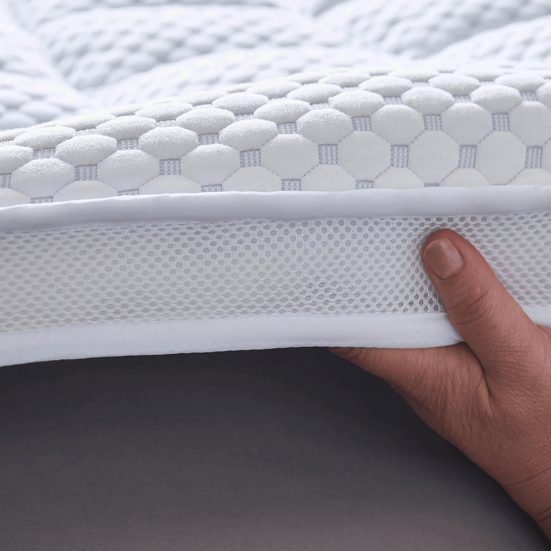 Hand holding a white mattress topper with textured surface and mesh side.