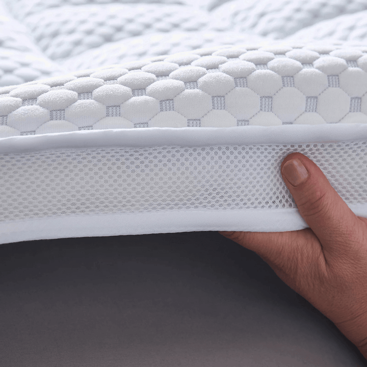 Hand holding a white mattress topper with textured surface and mesh side.
