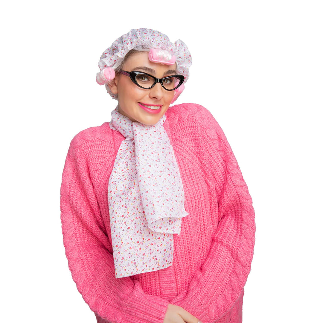 Woman wearing an old maid hat with pink rollers, pink cardigan, floral scarf and cats eyes glasses