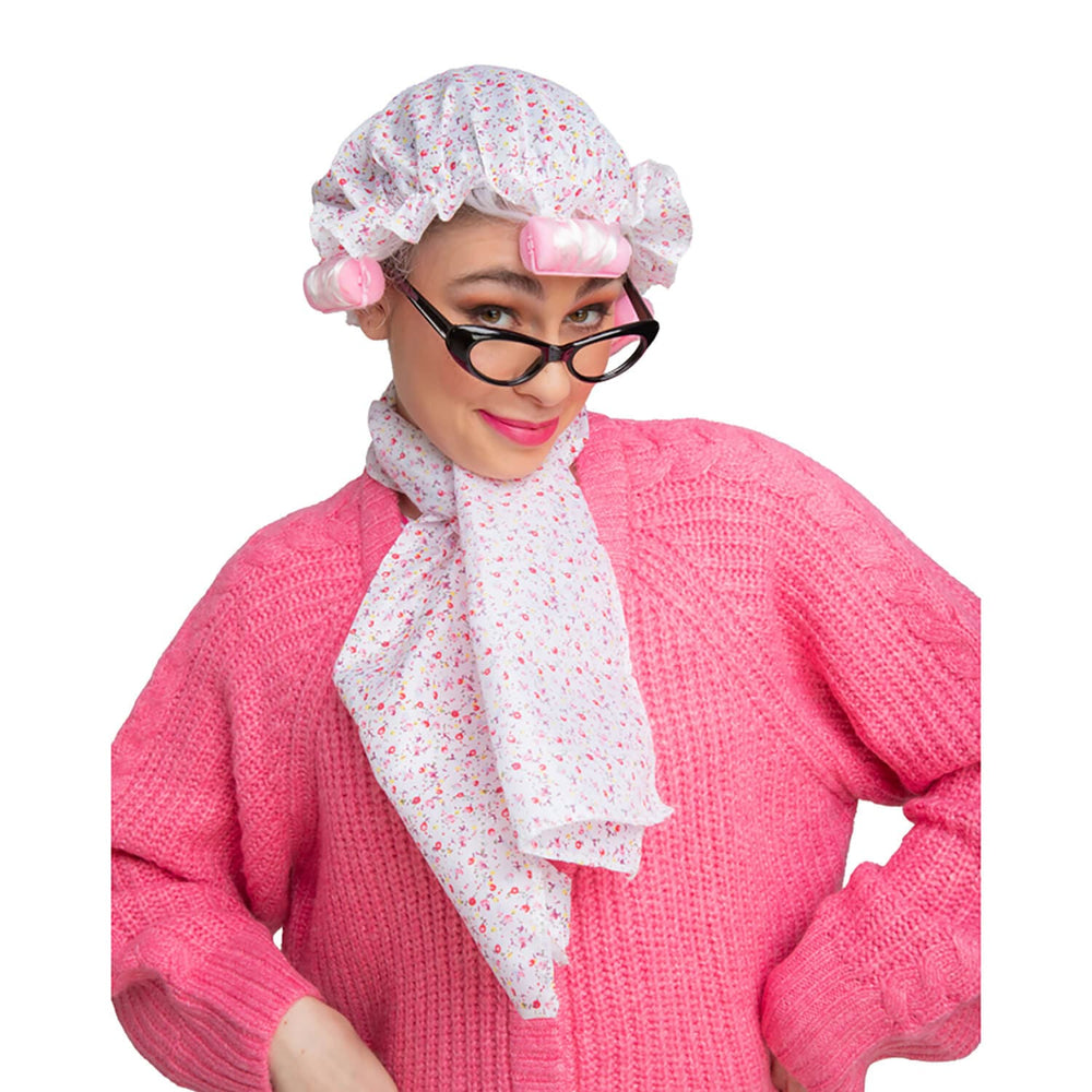 Person wearing a pink outfit with a shower cap with pink hair rollers and glasses on a white background