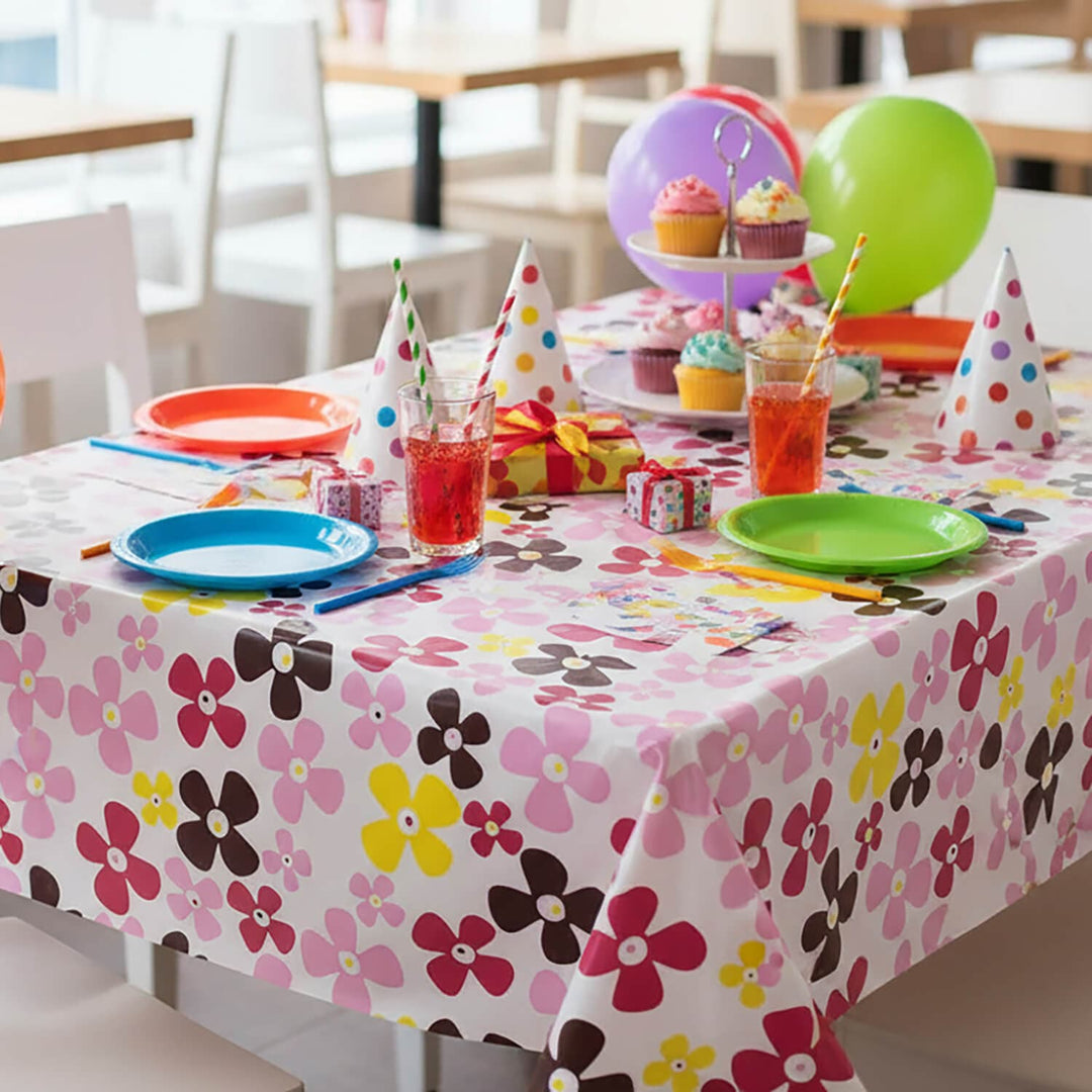 Children's birthday party setup with colourful flower pattern tablecloth, plates, cups, and balloons.