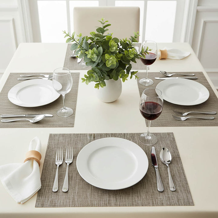 Dining table set with 4 coffee colour place mats, white plates cutlery and foliage centre piece