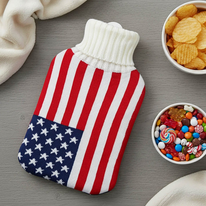 Hot water bottle with a USA flag cover on a grey table with crisps and sweets