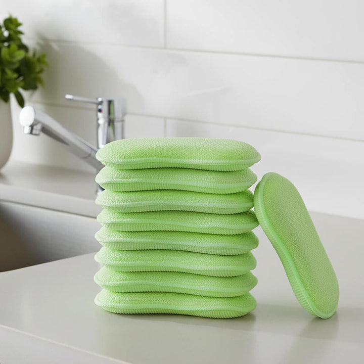 Stack of green cleaning pads on a kitchen worktop with sink tap and house plant