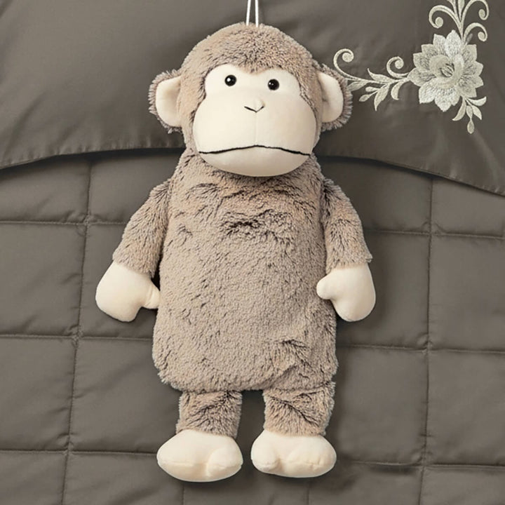 Plush monkey hot water bottle lying on a quilted bed cover with floral design.