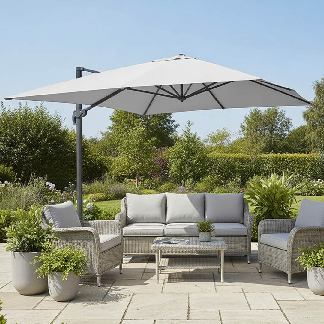Large silver garden parasol shading a grey rattan sofa set on a patio in the sun