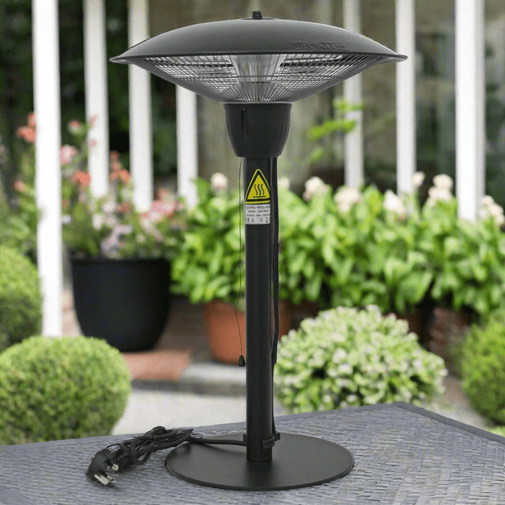 A black Azuma 1500w patio heater with a halogen tube, standing on a table with a garden in the background.