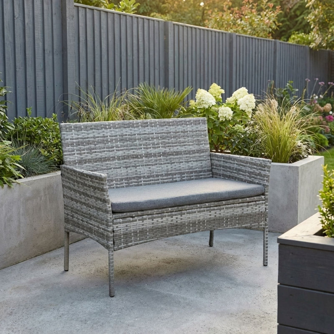 grey rattan bench on grey concrete patio with darker grey fence in background