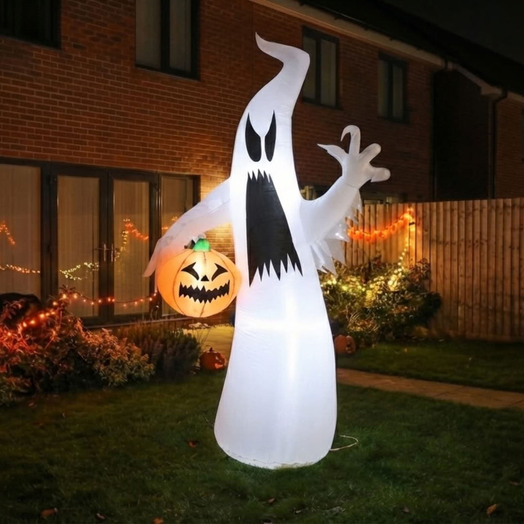 A large inflatable ghost Halloween decoration stands on a lawn in front of a house at night, glowing with warm light. The ghost is white with a black mouth and eyes, and a jack-o'-lantern pumpkin sits beside it.