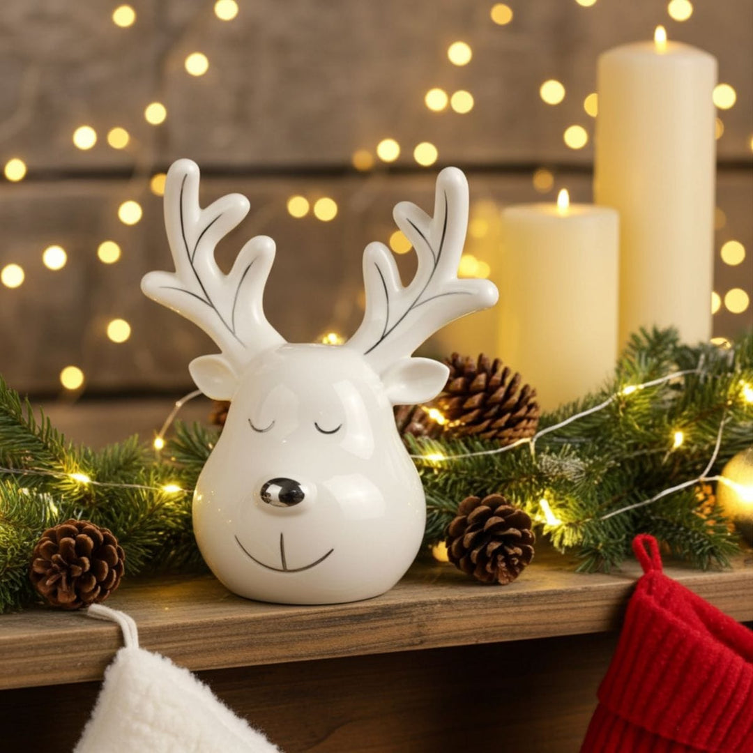 White reindeer-shaped ornament on a shelf with Christmas decorations and lights in the background.