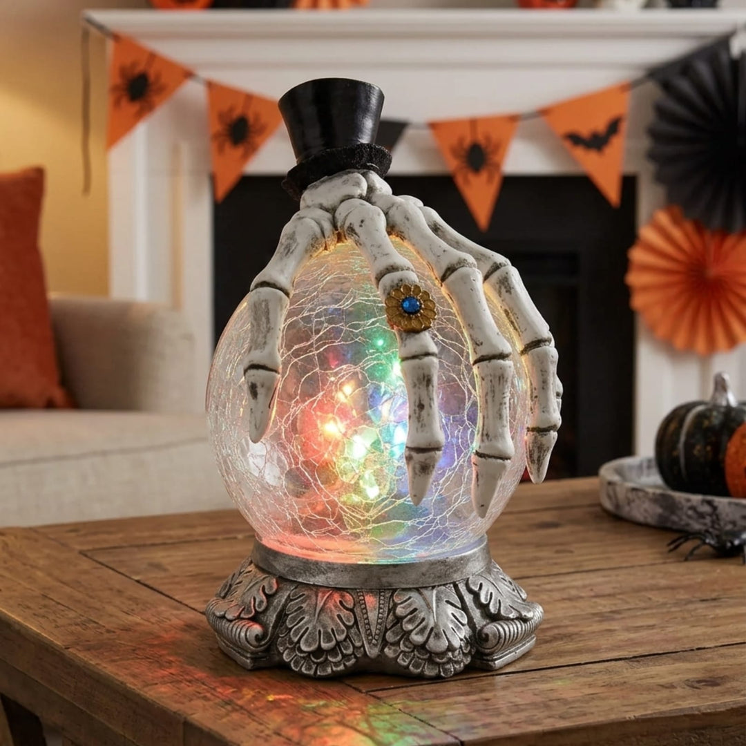 skeleton hand decoration on light up colour changing crackle glass glove on wooden coffee table in living room with halloween bunting in background