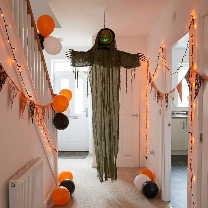 A Halloween hallway decoration featuring a hanging green scarecrow figure with outstretched arms and a glowing jack-o&