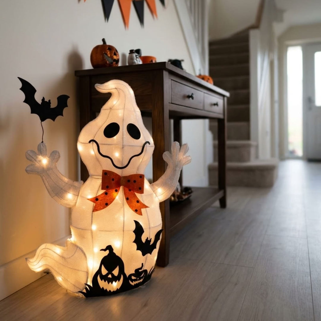 A glowing Halloween ghost floor decoration with integrated string lights, black bat cutouts, and jack-o'-lantern details, displayed in a home hallway next to a wooden console table.