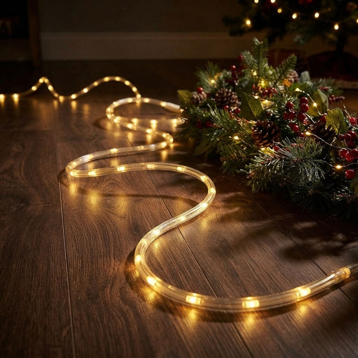 Warm white LED rope lights coiled on a dark wood floor next to a decorated Christmas wreath.