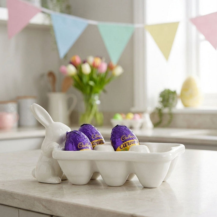 White ceramic bunny-shaped egg holder with Cadbury eggs on a kitchen counter, decorated with pastel-colored bunting.