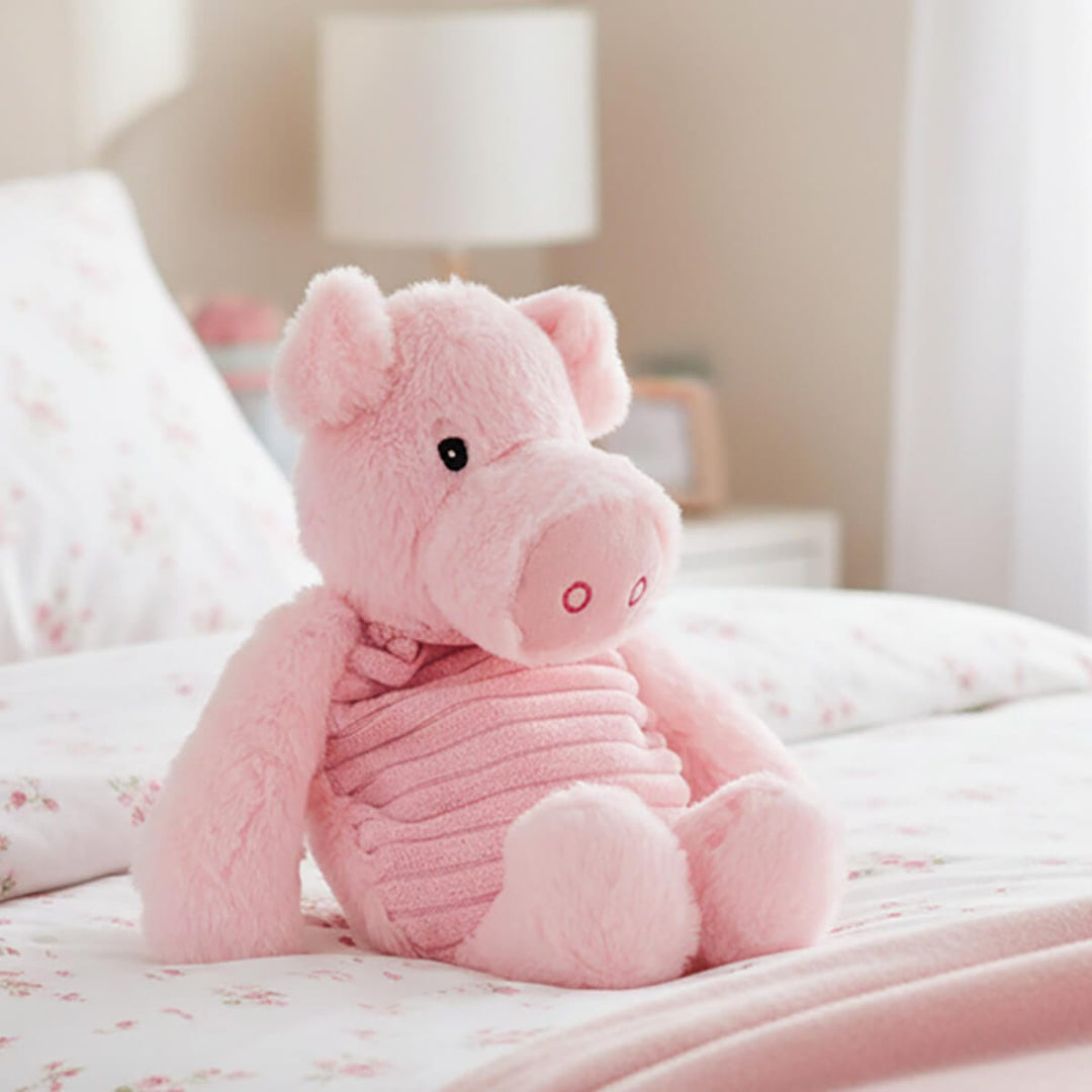 Pink plush pig heat pack sitting on a bed cover