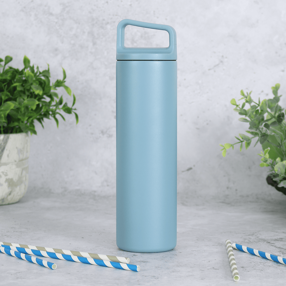 blue stainless steel water bottle with carry handle lid on concrete surface with plants in the background and grey and blue striped straws in the foreground