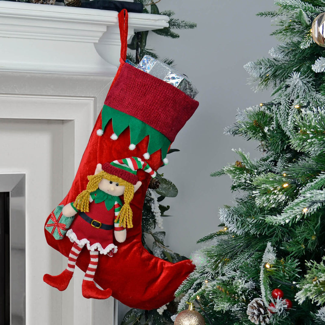 Red Christmas stocking with an elf design hanging on a fireplace next to a decorated tree.