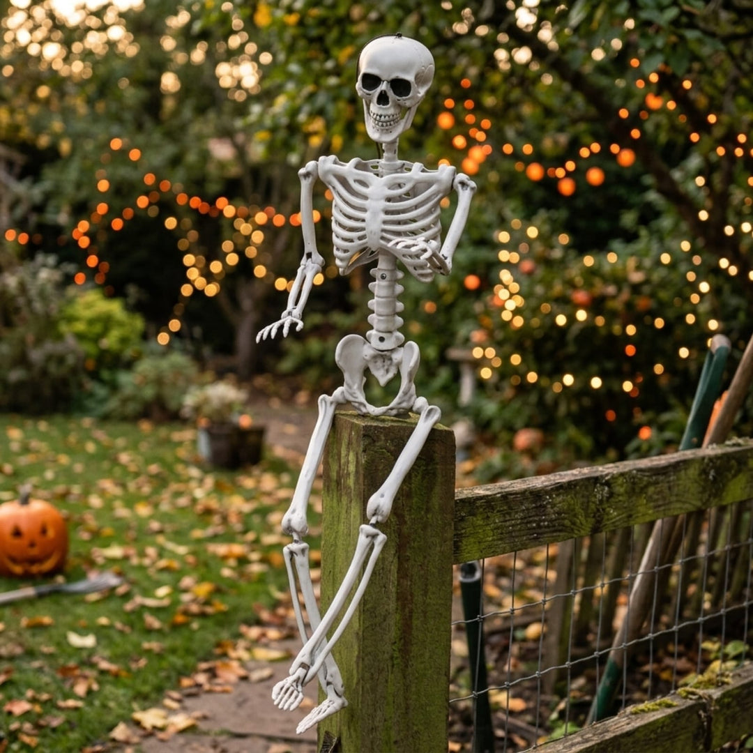poseable skeleton decoration resting on fence post in autumn garden with orange fairy lights hanging from trees and bushes in background