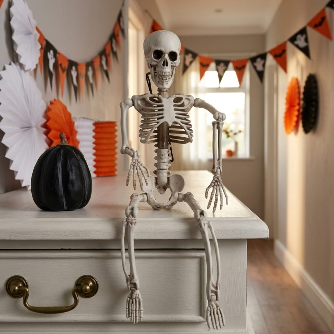 A posed plastic skeleton decoration sitting on a white dresser in a decorated hallway with Halloween banners, paper fans, and orange-and-black pennants.