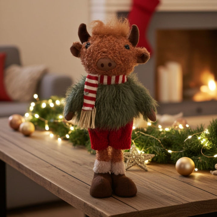 Plush toy cow in a festive outfit on a table with Christmas decorations.