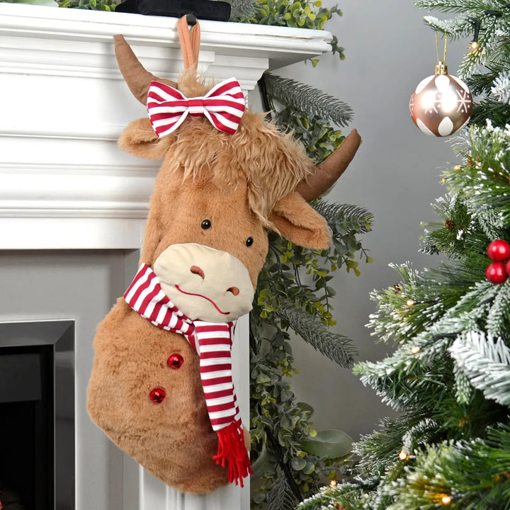 Highland Cow shaped Christmas stocking with a bow and scarf hanging on a fireplace mantle.