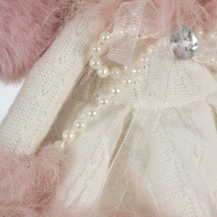 Close-up of a decorative item with pearls, ribbons, and crystals on a soft pink background.