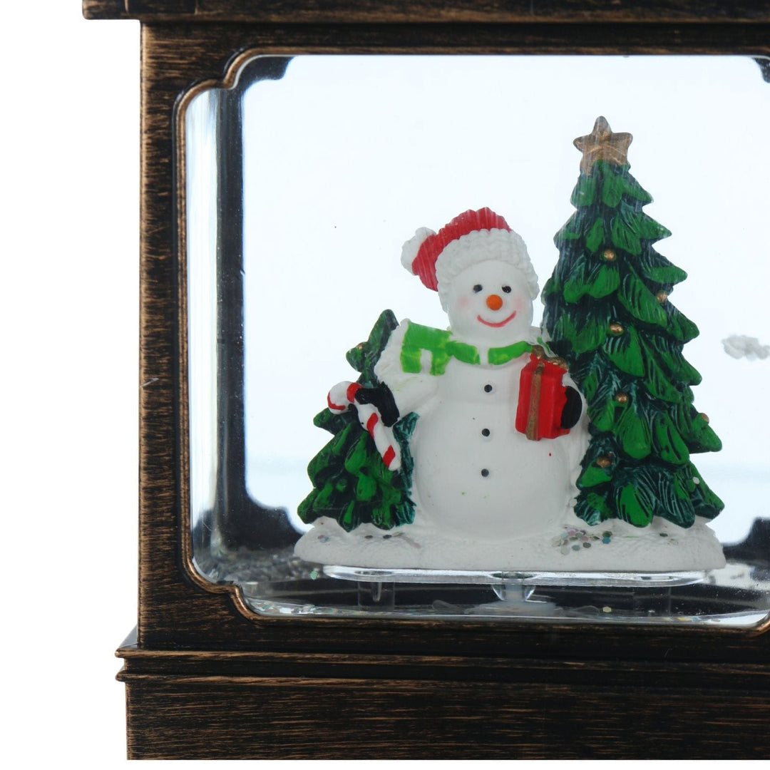 Decorative snowman with a tree and gift in a glass lantern display case.